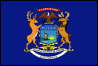 Image of the Michigan State Flag.  The flag displays the Michigan coat of arms on a field of blue. Depicted on the shield is a lake with a yellow sun rising over the blue waters. A man is standing on a peninsula with one hand raised in a greeting of friendship and the other hand holding a rifle. An Elk and a Moose support the shield between them and a Bald Eagle grasping an olive branch and arrows in its talons is shown above the shield. Three mottos are shown on the coat of arms: on a red ribbon - 'E Pluribus Unum' (From many, one); on a blue shield - 'Tuebor' (I will defend); and on a white ribbon - 'Si Quaeris Peninsulam Amoenam Circumspice' (If you seek a pleasant peninsula, look about you). These mottos are reflected in the coat of arms pictorially. 'E Pluribus Unum,' the national motto, aligns with the depiction of the Bald Eagle. 'Tuebor' is represented in the arrows clasped in the eagle's talons and the gun held in the man's left hand. 'Si Quaeris Peninsulam Amoenam Circumspice' is supported by the warmth of the sun, the man's friendly greeting from the peninsula and the olive branches held by the Bald Eagle. The Bald Eagle represents the United States and the Elk and Moose represent Michigan. The flag was adopted in 1911.