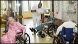 Picture showing residents in wheelchairs with attendant in nursing facility.