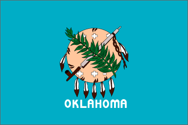Image of the Oklahoma State Flag.  The flag prominently displays an Osage warrior's shield made from buffalo hide and decorated with seven eagle feathers hanging from the lower edge. The shield is centered on a field of blue borrowed from the blue flag that Choctaw soldiers carried during the Civil War. This flag honors more than 60 groups of Native Americans and their ancestors. The shield is decorated with six white crosses (Native American signs for stars) representing high ideals. Superimposed over the shield are symbols of peace and unity from the cultures of the Native American and European-American settlers in the territory; the calumet or ceremonial peace pipe and the olive branch. The flag design was revisited in 1941. The state name 'OKLAHOMA' was ammended to the 1925 design and is displayed in white letters below the shield. This change was not popular in some circles as it was felt that the design of the Oklahoma State Flag was significantly unique without this reminder. In 1988, the Oklahoma State Legislature again addressed the design of the state flag. Variations in color among manufacturers did not properly align with the spirit of the design and the 41st Oklahoma Legislature voted to rectify this. The flag was adopted in 1925, and amended in 1941 and 1988.