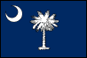 Image of the South Carolina State Flag.  The South Carolina State Flag is one of the oldest state flag designs still in use. Dating back to 1765, the flag reminds us of its role in the American Revolution and maintains its place in the annals of the Civil War with a design that was formulated as a National banner when the state seceded from the union on December 20, 1860. Components of the current state flag were first seen in 1765, on a banner carried by South Carolina protesters of the Stamp Act. The banner that the protesters hoisted displayed three white crescents on a blue background. Ten years later in 1775, Colonel William Moultrie was asked by the South Carolina Revolutionary Council of Safety to design a banner for the use of South Carolina troops. Colonel Moultrie chose a simple and direct design that displayed the crescent (new moon) on a blue field. The new flag was the same blue color of the soldiers' uniforms and the silver crescent echoed the symbol that the soldiers wore on the front of their caps. Almost 100 years later, South Carolina seceded from the Union it had fought to create. A new banner was needed to fly above the newly created nation. Many designs were reviewed but the General Assembly settled on one simple change to Moultrie's Revolutionary War design. A Palmetto tree was added and centered on the blue field. The Palmetto, the South Carolina State Tree, had been attributed as instrumental in Colonel Moultrie's defense of Sullivan's Island against an attack by British warships in June, 1776. Cannonballs fired at the fort from the British ships could not destroy the walls of the fort which were built of Palmetto logs. Instead, the cannonballs simply sank into the soft, tough Palmetto wood. The flag that flies over the state of South Carolina today is of the same design that flew over the independent South Carolina during the Civil War. The flag was adopted in 1861.
