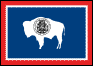 Image of the Wyoming State Flag.  The flag displays a bison, the Wyoming State Mammal often called the monarch of the plains, centered on the flag. Branded on the white-colored bison is the Great Seal of Wyoming. The bison faces the staff, and is placed on a large field of blue. The blue field has a small edging of white, seperating it from a band of red at the outer edge of all four sides of the flag. The most prominent feature of Wyoming's seal is the central figure of a woman standing before a banner which reads 'Equal Rights'. Wyoming bears the honorable distinction of being at the forefront of states advocating equal rights for men and women, well before the turn of the century. On either side of the female figure are two pillars, each with scrolls that proclaim Wyoming's major economic strengths: oil, mines, livestock, and grain. On each pillar are burning lamps, symbolizing the Light of Knowledge. In the foreground, a striped shield and star, topped by an eagle, represent Wyoming's sovereignty and dedication to the Union. The number 44 identifies Wyoming as the 44th state to enter the Union. On either side of a shield are the dates 1869 and 1890, which represent, respectively, the date that Wyoming organized as a Territory, and the date that Wyoming gained statehood. Flanking the pillars are figures representing the livestock and mining industries. An outer circle bears the words 'The Great Seal of the State of Wyoming'. The colors of the State Flag are the same as those of the National Flag. The red border represents the Indians who knew and loved the country long before the settlers came.; also the blood of the pioneers who gave their lives reclaiming the soil. White is the emblem of purity and uprightness over Wyoming. Blue, the color of the sky and mountains, is symbolic of fidelity, justice and virility. The flag was adopted in 1917.
